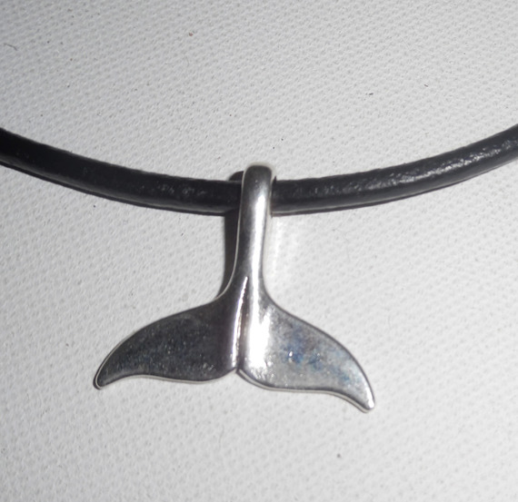 Pingente de cauda de golfinho sortudo em metal prateado sobre pele preta