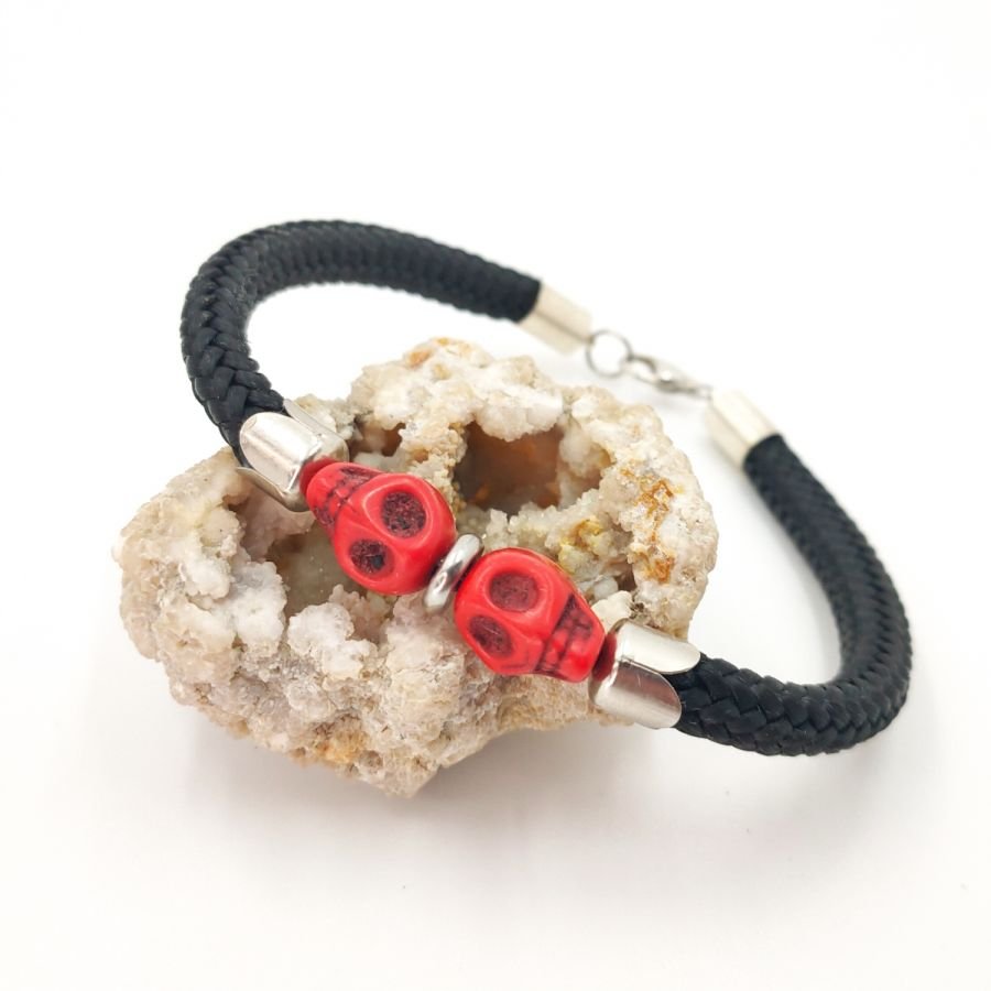 Crânio duplo e bracelete de ossos cruzados com pedras vermelhas numa corda preta espessa