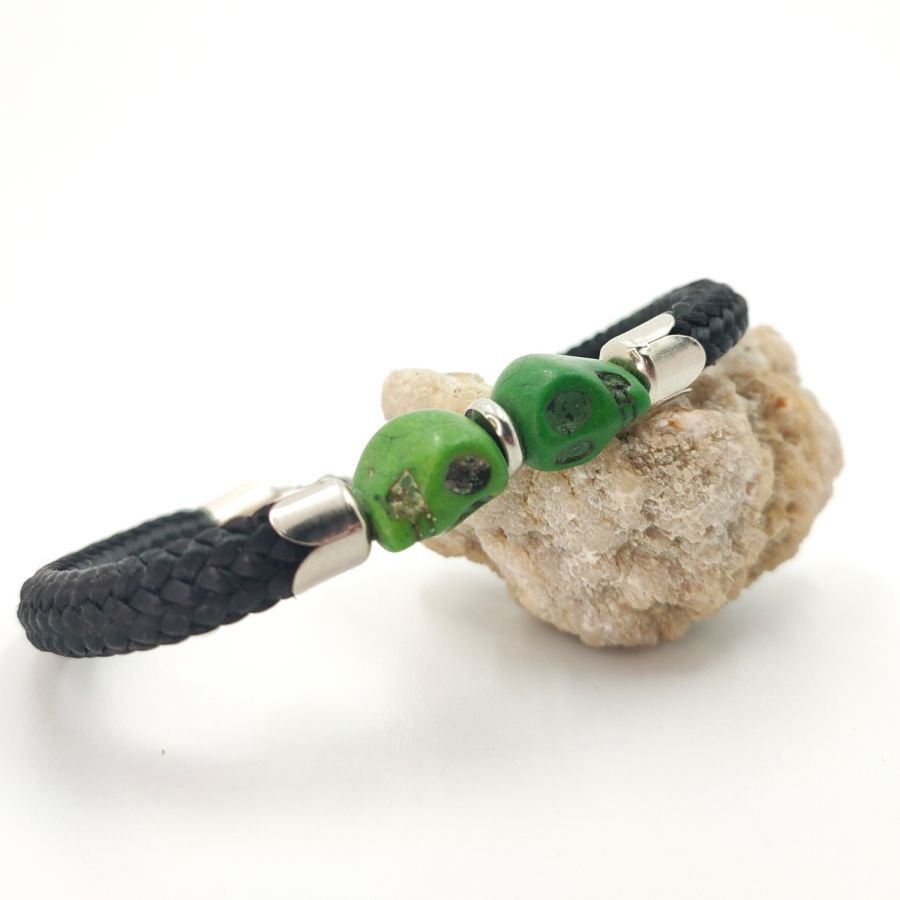 Crânio duplo e bracelete de ossos cruzados com pedras verdes sobre corda preta